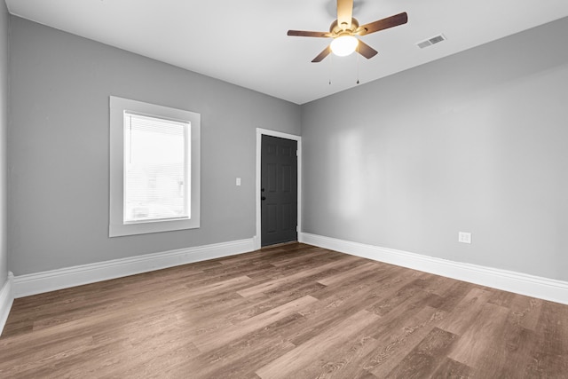 empty room featuring ceiling fan, visible vents, baseboards, and wood finished floors