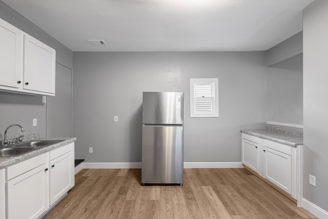 kitchen with visible vents, freestanding refrigerator, light wood-style floors, white cabinetry, and a sink