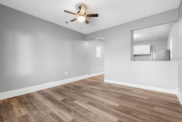 spare room featuring a ceiling fan, visible vents, wood finished floors, and baseboards