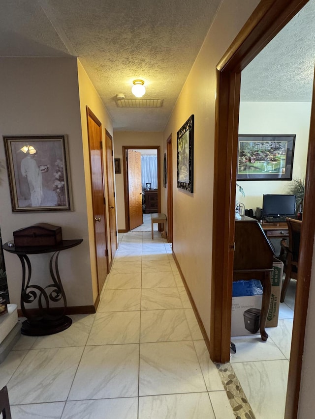 hallway with visible vents, baseboards, a textured ceiling, and marble finish floor