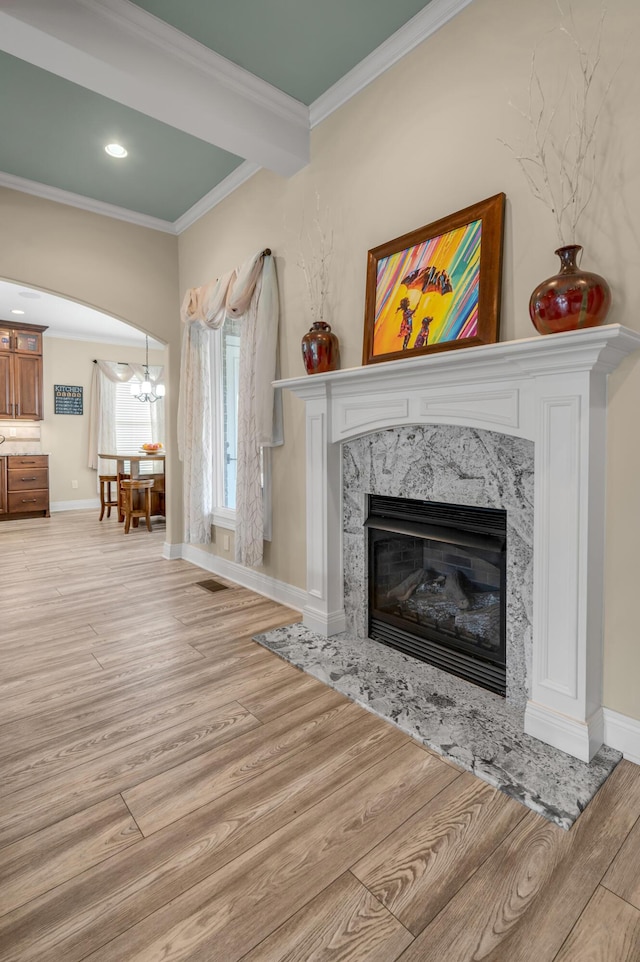 living area featuring baseboards, arched walkways, ornamental molding, wood finished floors, and a fireplace