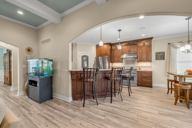 kitchen featuring arched walkways, brown cabinets, a kitchen breakfast bar, stainless steel appliances, and under cabinet range hood