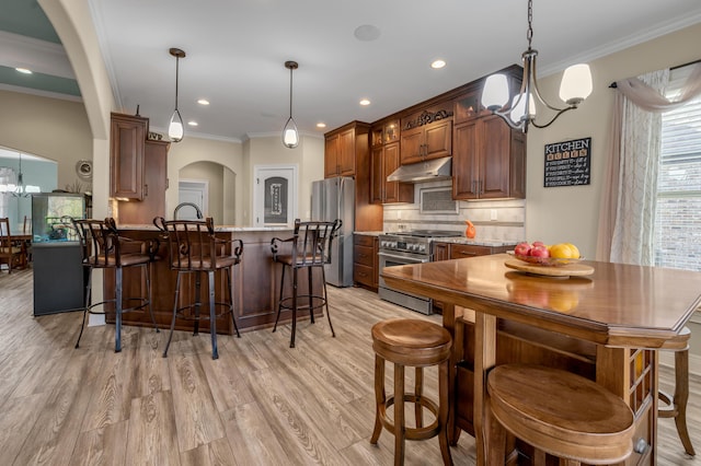 kitchen with stainless steel appliances, a chandelier, under cabinet range hood, and backsplash