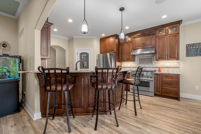 kitchen featuring arched walkways, under cabinet range hood, refrigerator, tasteful backsplash, and stainless steel range