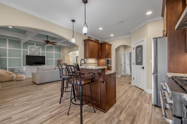 kitchen with light wood finished floors, a breakfast bar area, arched walkways, and a ceiling fan