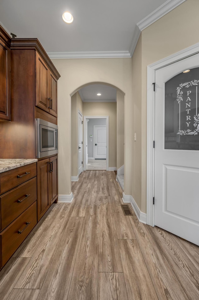 interior space with light wood-type flooring, arched walkways, stainless steel microwave, and ornamental molding