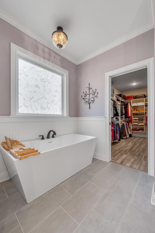 full bath with ornamental molding, a walk in closet, a freestanding tub, and wainscoting