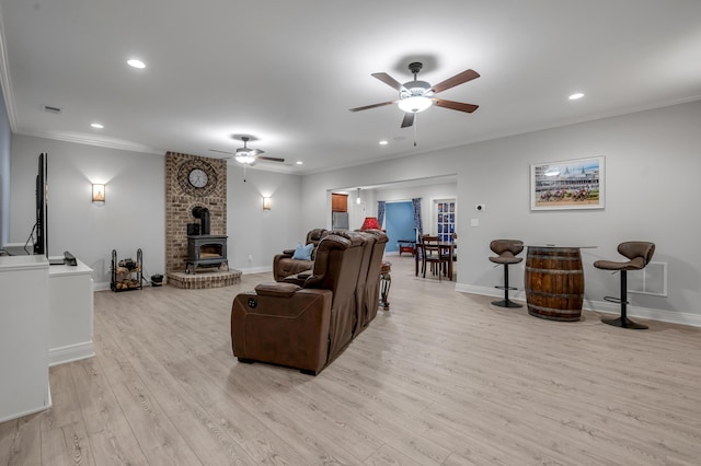 living room with recessed lighting, baseboards, light wood finished floors, a wood stove, and crown molding