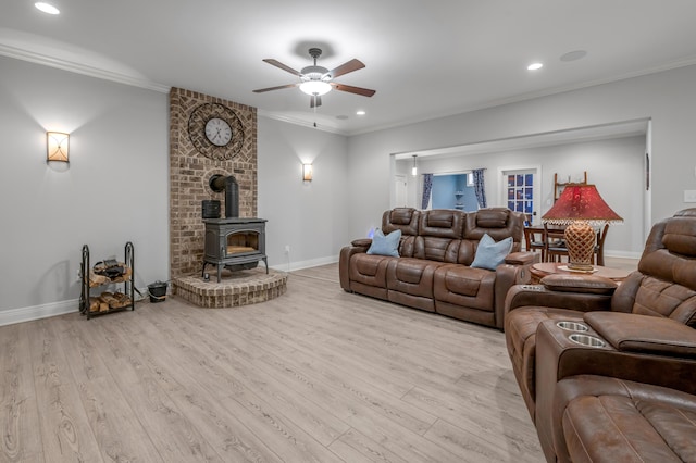 living area with ornamental molding, a wood stove, ceiling fan, wood finished floors, and baseboards