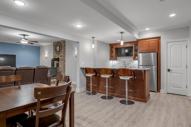 kitchen with a kitchen breakfast bar, freestanding refrigerator, a peninsula, light stone countertops, and backsplash