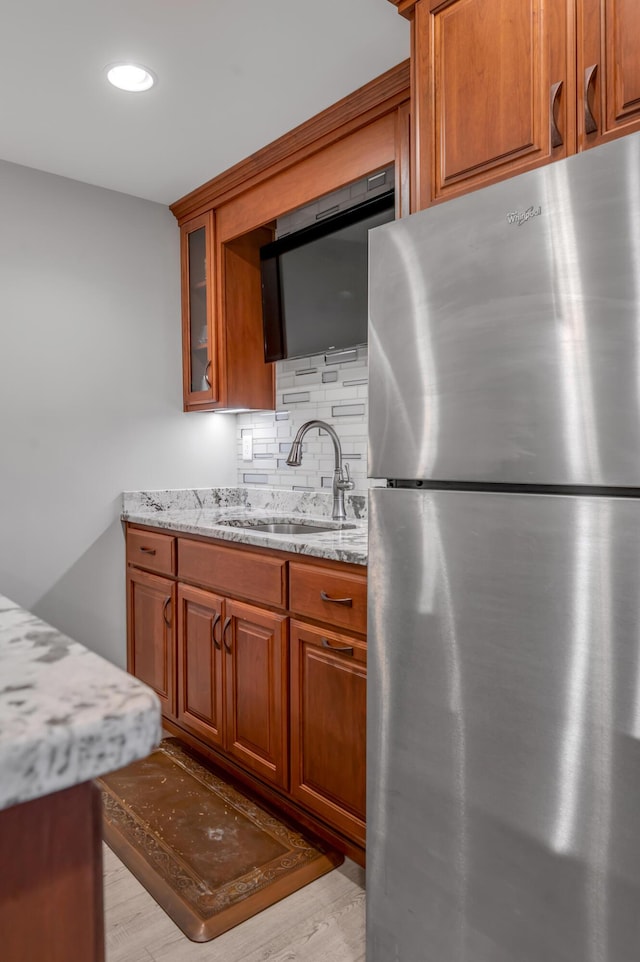 kitchen with tasteful backsplash, brown cabinetry, light stone counters, freestanding refrigerator, and a sink