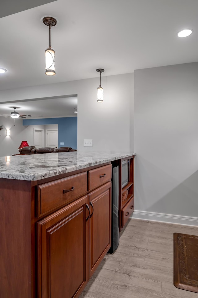 kitchen featuring hanging light fixtures, light stone counters, brown cabinetry, and light wood-style flooring