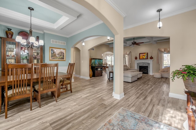 dining room featuring light wood finished floors, visible vents, arched walkways, a premium fireplace, and ceiling fan with notable chandelier