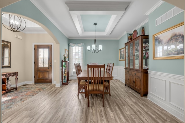 dining area featuring a chandelier, arched walkways, wainscoting, light wood finished floors, and a raised ceiling