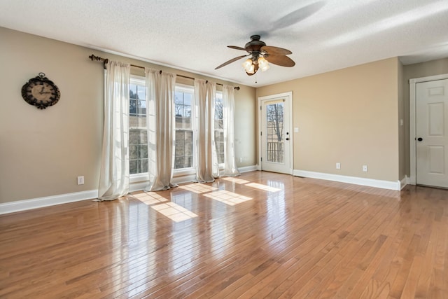 empty room featuring light wood finished floors, a ceiling fan, baseboards, and a textured ceiling