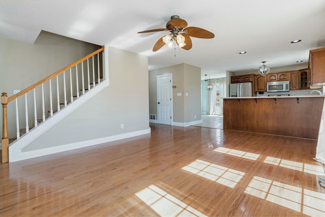 unfurnished living room with light wood finished floors, visible vents, stairway, baseboards, and ceiling fan with notable chandelier