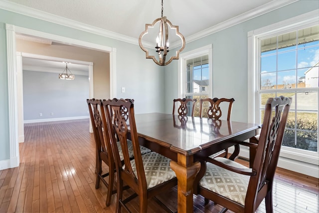 dining area with crown molding, a healthy amount of sunlight, wood-type flooring, and an inviting chandelier