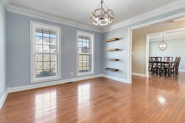 unfurnished room featuring baseboards, visible vents, ornamental molding, hardwood / wood-style floors, and an inviting chandelier