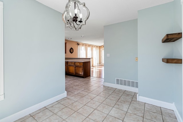 unfurnished room featuring an inviting chandelier, baseboards, light tile patterned floors, and visible vents