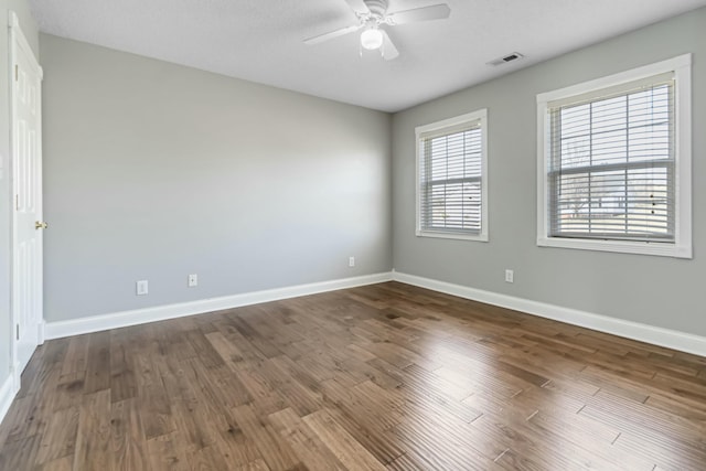 empty room featuring a ceiling fan, dark wood-style flooring, visible vents, and baseboards