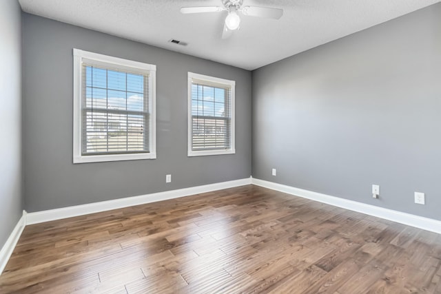 empty room with baseboards, visible vents, a ceiling fan, wood finished floors, and a textured ceiling