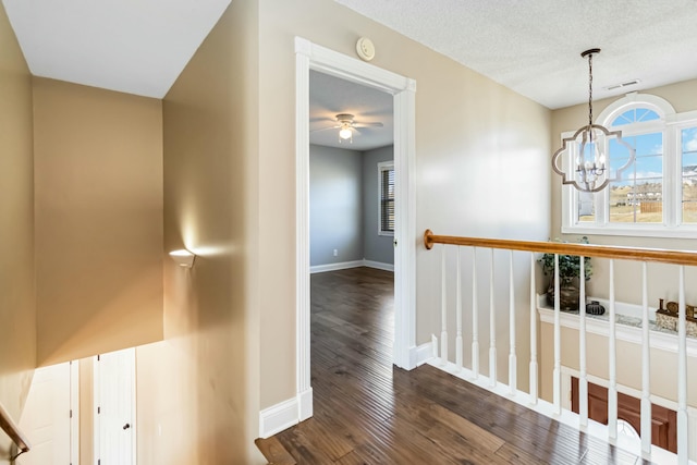 hallway featuring dark wood-style flooring, a textured ceiling, baseboards, and an inviting chandelier