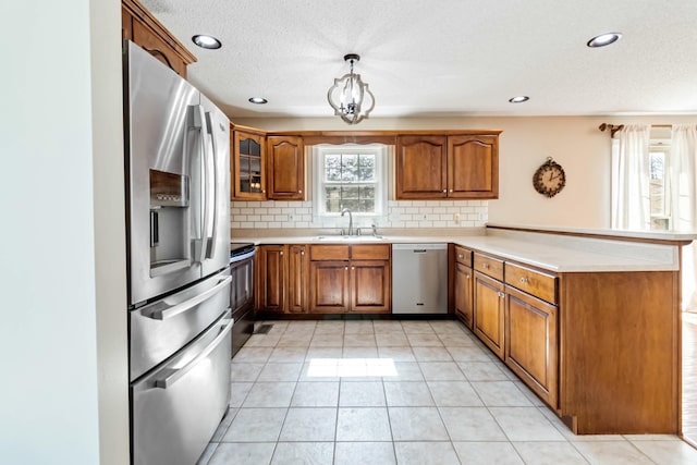 kitchen with stainless steel appliances, brown cabinetry, a sink, and a peninsula