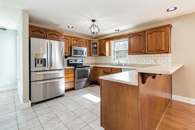 kitchen featuring a peninsula, appliances with stainless steel finishes, decorative backsplash, and a sink