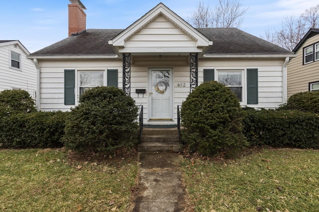 bungalow featuring a front yard, roof with shingles, and a chimney