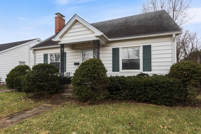 bungalow-style home with a chimney, a front yard, and a shingled roof