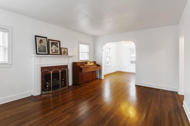 unfurnished living room featuring arched walkways, dark wood-style flooring, visible vents, a tile fireplace, and baseboards