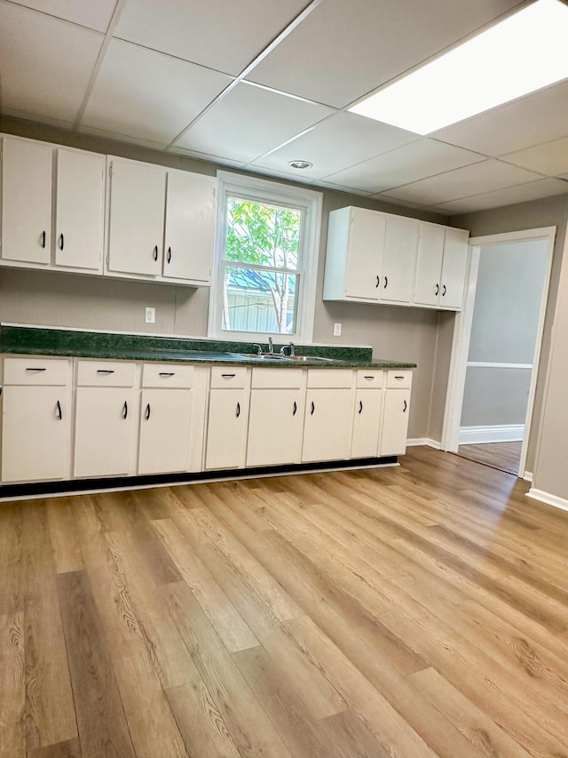 kitchen featuring light wood-type flooring, dark countertops, a paneled ceiling, and white cabinets