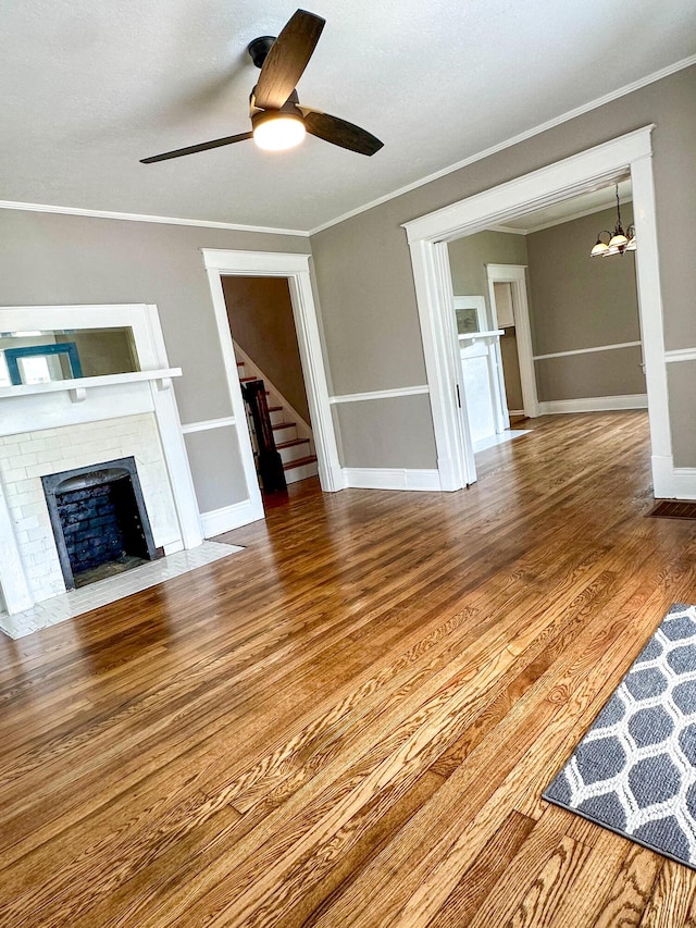 unfurnished living room with ceiling fan with notable chandelier, a fireplace, wood finished floors, stairs, and ornamental molding