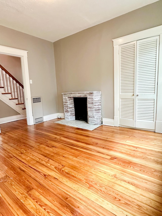 unfurnished living room with stairs, a stone fireplace, baseboards, and wood finished floors