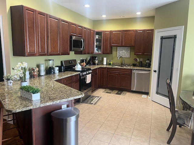 kitchen with light tile patterned floors, a breakfast bar, a peninsula, a sink, and appliances with stainless steel finishes