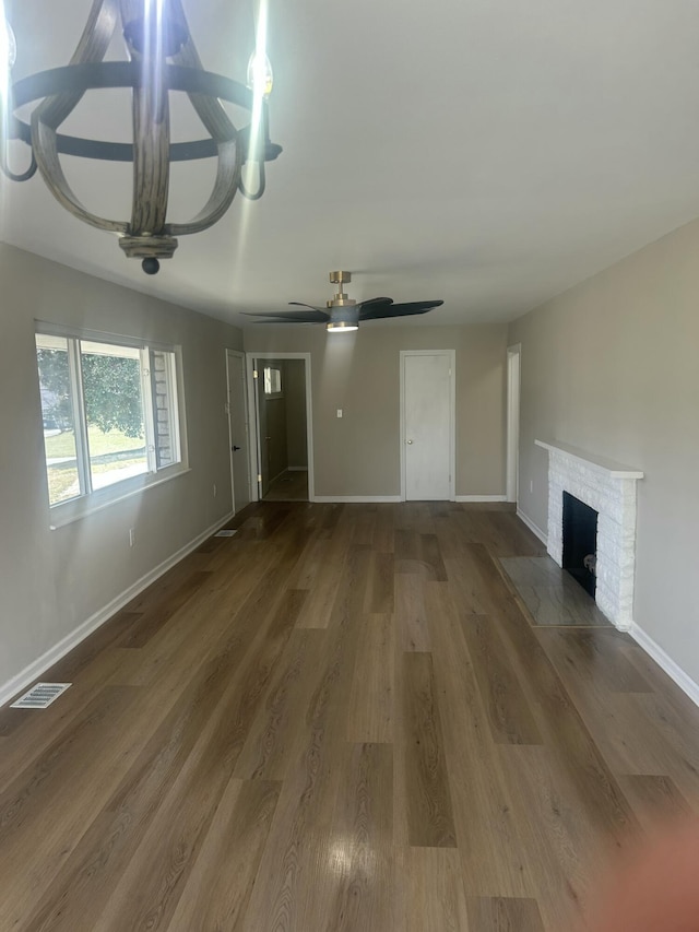 unfurnished living room featuring ceiling fan, wood finished floors, visible vents, baseboards, and a brick fireplace