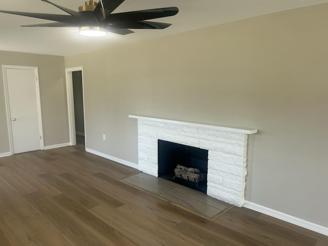 unfurnished living room with dark wood-type flooring, a fireplace, baseboards, and a ceiling fan