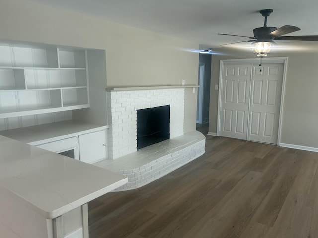 unfurnished living room with a brick fireplace, ceiling fan, baseboards, and wood finished floors