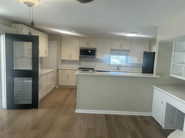 kitchen featuring black refrigerator, wood finished floors, a sink, light countertops, and stainless steel microwave