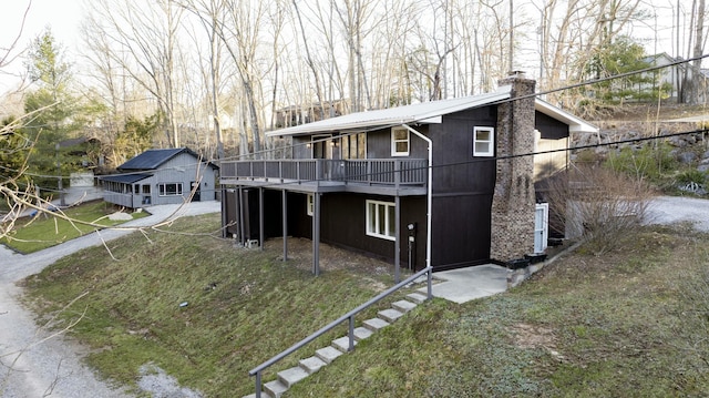 view of front of home with a wooden deck, stairs, a front yard, a chimney, and metal roof