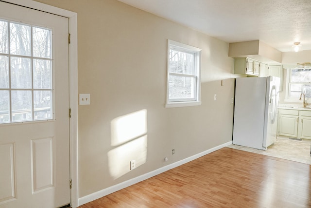 kitchen with a sink, light wood-type flooring, white fridge with ice dispenser, and a wealth of natural light