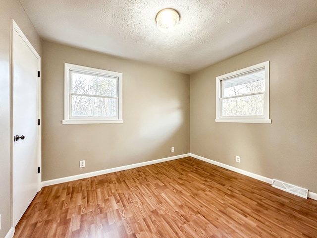 unfurnished room featuring baseboards, visible vents, a wealth of natural light, and light wood-type flooring