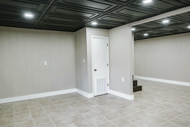 finished basement with light tile patterned floors, visible vents, baseboards, and an ornate ceiling