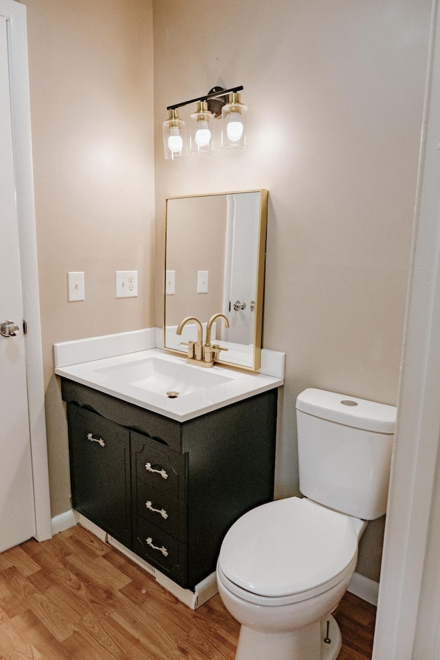 half bath featuring toilet, vanity, baseboards, and wood finished floors