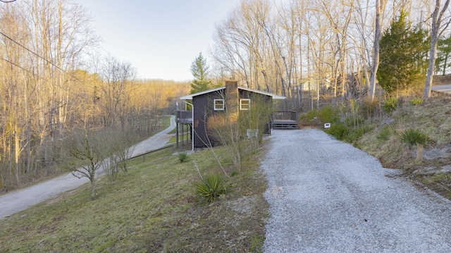 exterior space with a chimney, a wooded view, and driveway