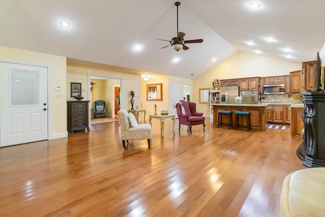 living area featuring light wood finished floors, ceiling fan, baseboards, and high vaulted ceiling