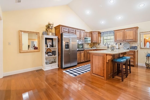 kitchen featuring light wood-style floors, light countertops, appliances with stainless steel finishes, decorative backsplash, and a kitchen bar