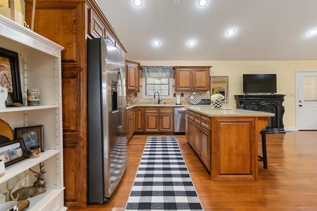 kitchen with a breakfast bar, brown cabinets, light countertops, appliances with stainless steel finishes, and a sink