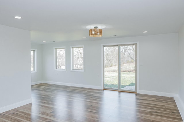 spare room featuring plenty of natural light, recessed lighting, baseboards, and wood finished floors