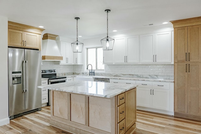 kitchen with a kitchen island, wall chimney range hood, light stone countertops, light wood-type flooring, and stainless steel appliances